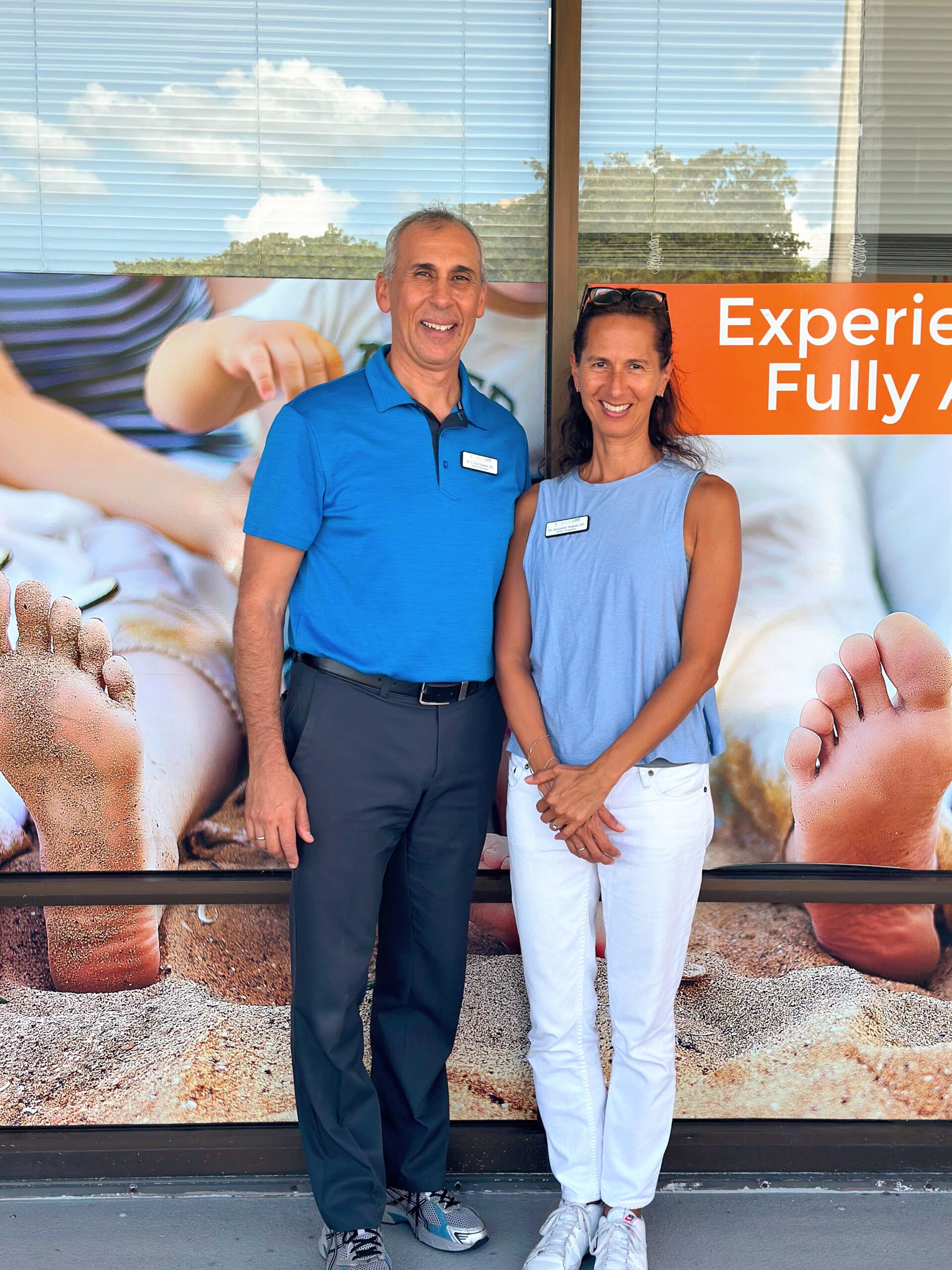 Dr. Gus Tsiapalis and Dr. Jacqueline Tsiapalis posing in front of Great Life Chiropractic, a family wellness center